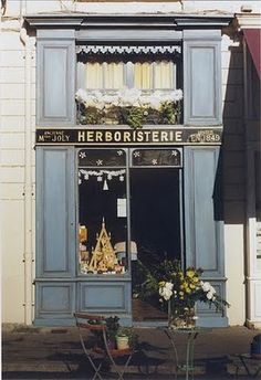 a store front with flowers and decorations on display in the window, next to a bench