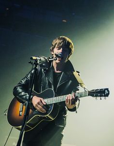 a man holding a guitar while standing in front of a microphone on top of a stage