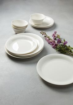 a table topped with plates and flowers on top of a gray countertop covered in white dishes