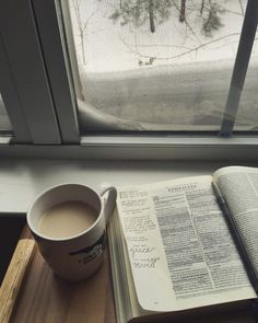 a cup of coffee and an open book on a table next to a window sill