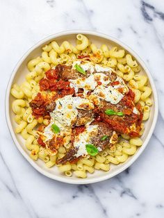 a white bowl filled with pasta and meat covered in sauce on top of a marble table