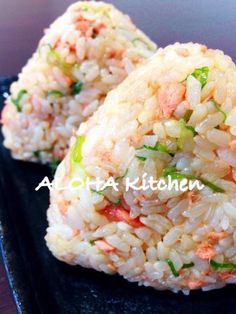 rice balls with vegetables and seasoning on top sit on a black plate, ready to be eaten