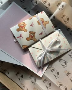 two cards with bows and teddy bears on them sitting next to each other in front of wrapping paper