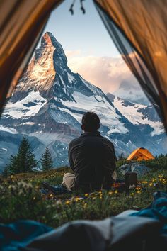 a man sitting in front of a tent on top of a mountain