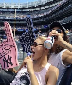 two women holding up signs in front of a crowd at a baseball game, one with her hand on the other's head