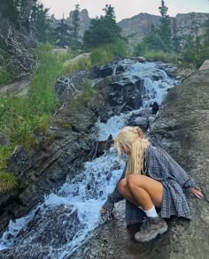 a woman sitting on top of a rock next to a river with water running down it