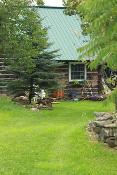 a log cabin sits in the middle of a grassy yard with trees and rocks around it