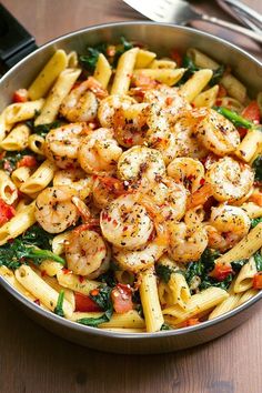 pasta with shrimp, spinach and tomatoes in a pan on a table next to silverware