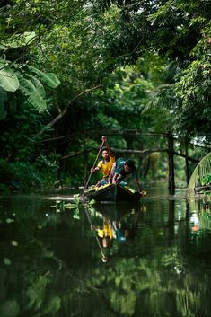 two people in a small boat on a body of water surrounded by trees and greenery