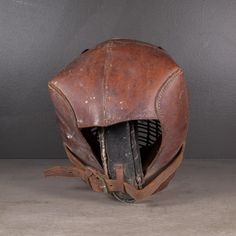 an old leather helmet sitting on top of a cement floor next to a gray wall