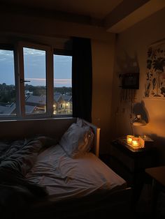 an unmade bed sitting next to a window in a room with two lamps on each side