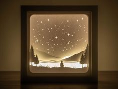 an origami night light with trees and stars in the sky, on a wooden table