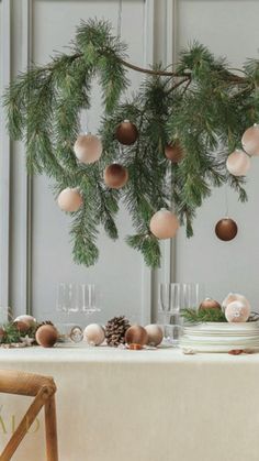 the table is set for christmas dinner with pine branches and ornaments hanging from the ceiling