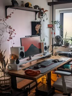 a desk with two computer monitors and speakers on it, in front of a window