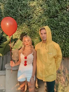 a man and woman in yellow raincoats standing next to each other holding red balloons