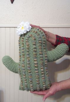 a person holding a crocheted cactus with a flower on it's back