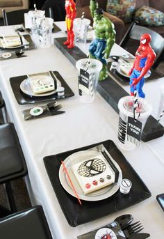 the table is set with black and white plates, silverware, and spiderman figurines