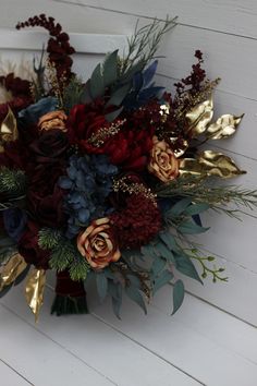 a bouquet of red and gold flowers on a white doorknoth with greenery