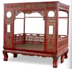 a red wooden bed with intricate carvings on the top and sides, against a white background