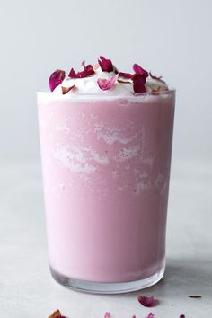 a glass filled with pink milk and topped with rose petale petals on a white surface