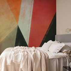 a bed with white sheets and pillows in front of a colorful painting on the wall