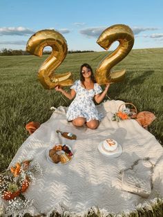 a woman sitting on top of a blanket holding two gold balloons in the shape of numbers