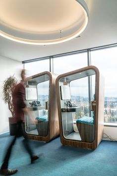 a man walking past two large mirrors in an office building with blue carpeted flooring