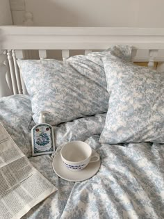 a cup and saucer sitting on top of a bed next to an open newspaper