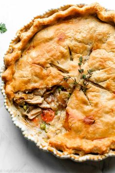 a chicken pot pie in a white dish on a marble surface with sprigs of rosemary