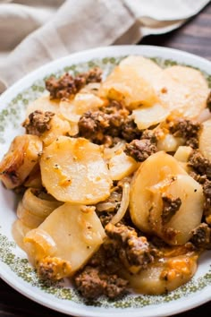 a white plate topped with potatoes covered in ground beef and meat sauce on top of a wooden table