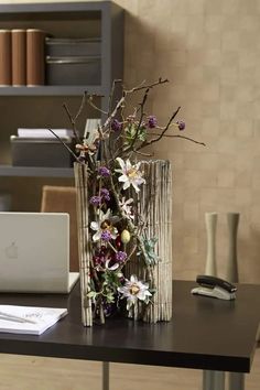 a desk with a laptop and flowers in a vase next to it on the table