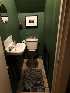 a small bathroom with green walls and white fixtures on the wall, along with a black rug