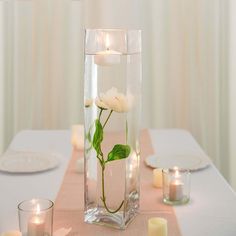 a vase filled with water and flowers on top of a table next to lit candles