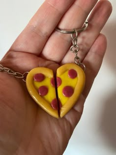 a hand holding a yellow heart shaped keychain with a slice of pizza on it