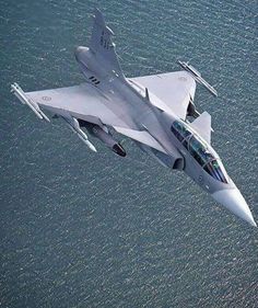 an aerial view of a fighter jet flying in the sky above the ocean with it's landing gear down