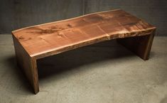 a wooden bench sitting on top of a cement floor in front of a gray wall