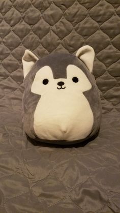 a gray and white stuffed animal sitting on top of a bed