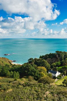 an aerial view of the ocean and green hills with trees on each side, in front of a blue sky