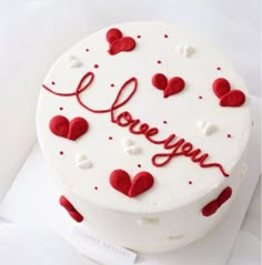 a white cake with red hearts and the words love you written on it in cursive writing