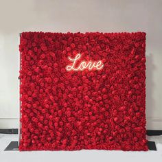 a red wall with the word love written on it and flowers in front of it