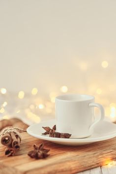 a white cup and saucer sitting on top of a wooden table next to cinnamons