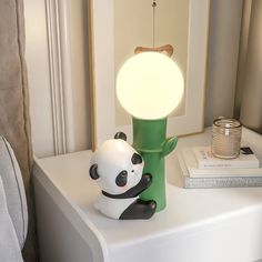 a panda bear lamp sitting on top of a white night stand next to a bed