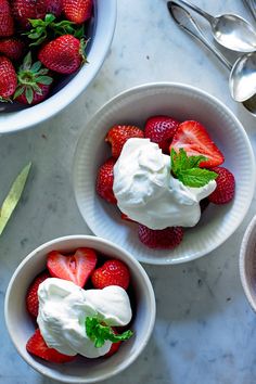 two bowls filled with whipped cream and strawberries on top of a marble countertop