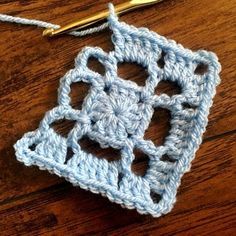 a crocheted square is shown with a golden knitting needle on the table next to it