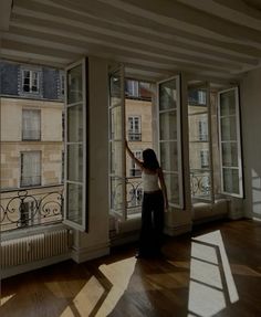 a woman is standing in an empty room with open windows and looking out onto the street