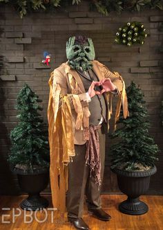 a man dressed up as a zombie standing in front of a brick wall with fake trees