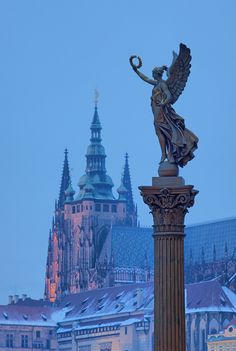 an angel statue on top of a pillar in front of a building with spires