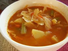 a white bowl filled with vegetable soup on top of a wooden table next to a red cloth