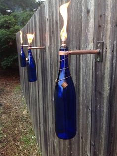 three blue glass bottles hanging from a wooden fence with fire coming out of the top