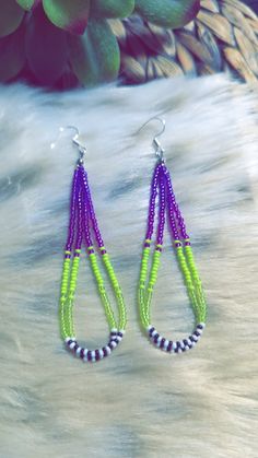 the neon green and purple beaded earrings are on top of a white fur rug